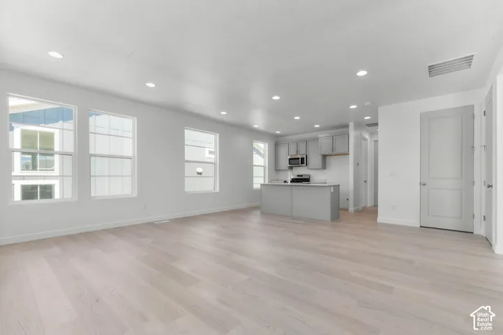 Open-concept living space featuring wood-finish flooring, recessed lighting, multiple windows, a kitchen island, and stainless steel appliances