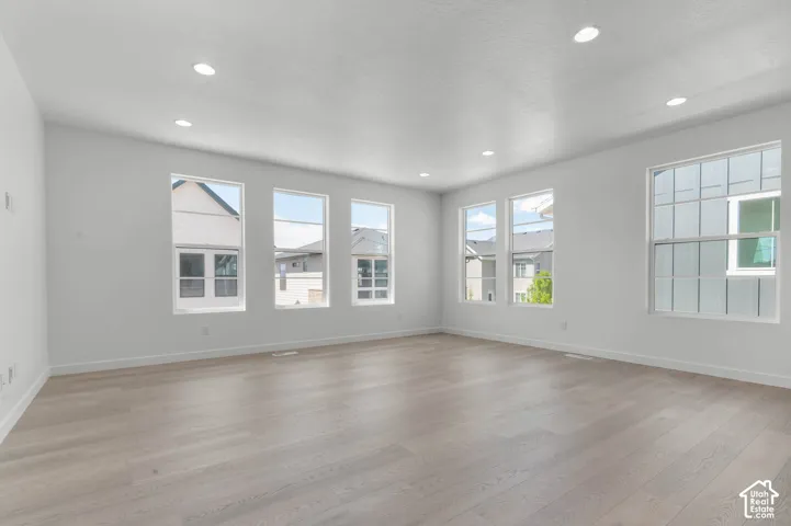 Recessed lighting illuminates an expansive room featuring light wood-finish flooring and multiple large windows
