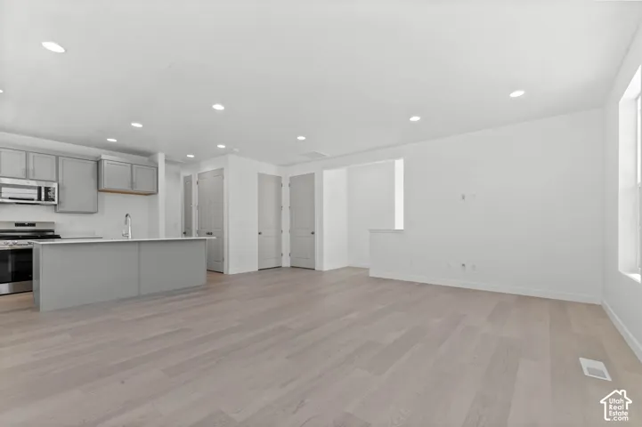 Open-concept living space featuring wood-finish flooring, recessed lighting, and a kitchen with stainless steel appliances, grey cabinetry, and a central island