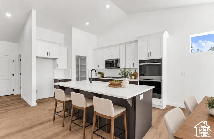 Kitchen featuring a large island with a solid surface countertop, wood-finish flooring, white cabinetry, integrated double ovens, and a built-in pantry