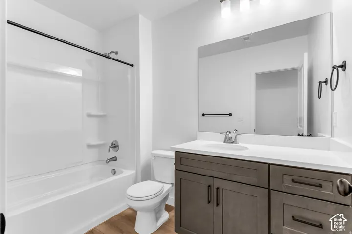 White bathtub with integrated shelving, brushed nickel fixtures, wood-finish flooring, dark wood-finish vanity with a white countertop, and a large wall-mounted mirror
