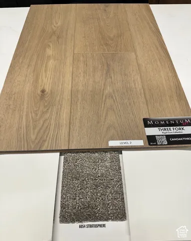 Wood-finish flooring planks featuring a natural grain texture, paired with textured gray carpeting and white solid-surface finish samples