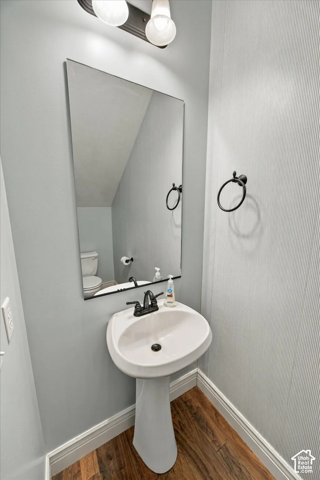 Pedestal sink with dark-toned fixtures, rectangular mirror, and wood-finish flooring