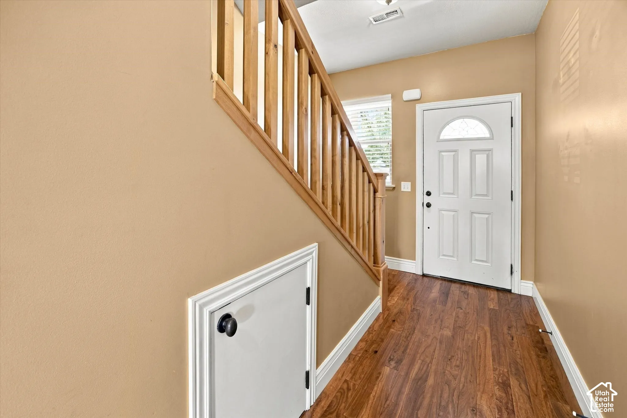 Wood-finish flooring leading to a white paneled entry door with an arched decorative glass insert