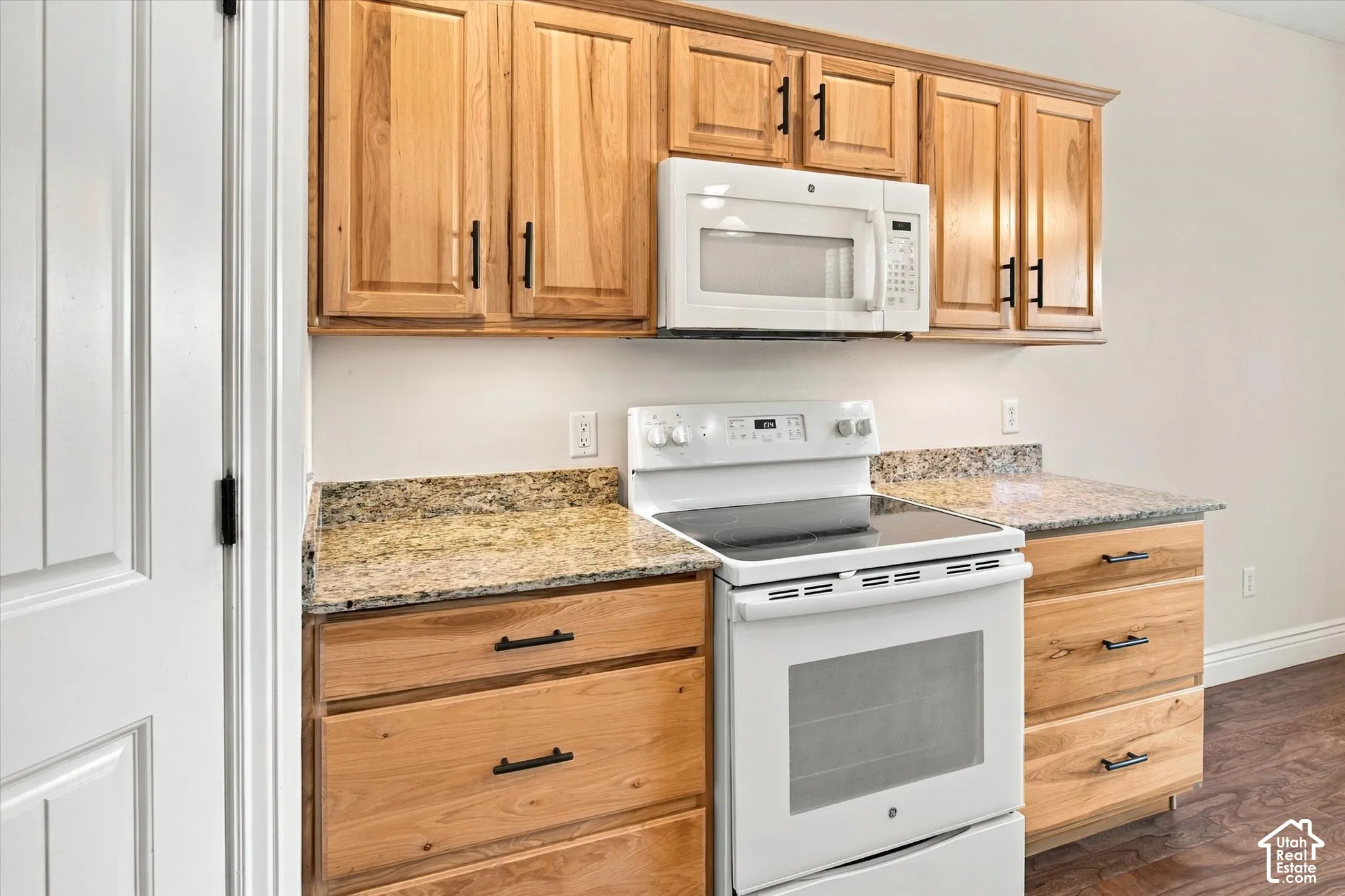 Hardwood cabinetry with matte black hardware, granite countertops, white electric range, and a built-in microwave