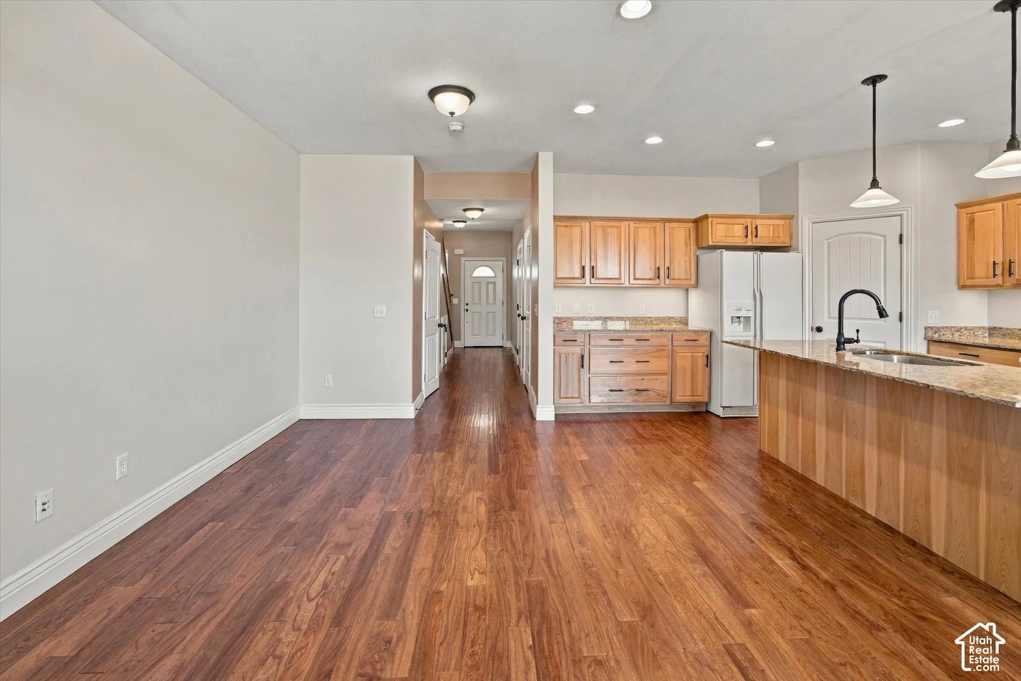 Wood-finish flooring throughout, kitchen with light wood cabinetry, stone countertops, and a white refrigerator