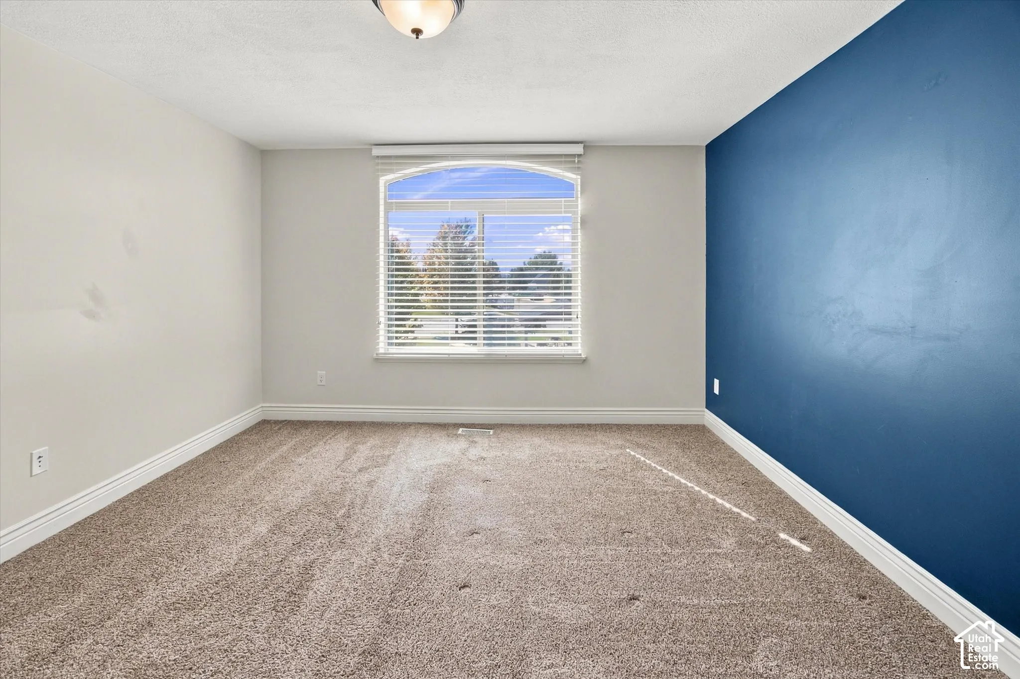 Arched window with blinds, recessed ceiling light, wall-to-wall carpeting, and a contrasting accent wall