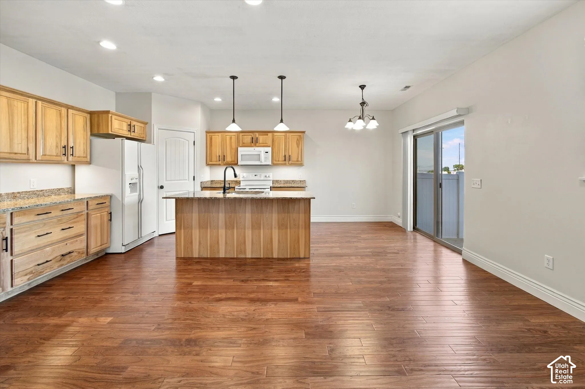 Open-concept kitchen and dining area featuring wood-finish flooring, light wood cabinetry, granite-style countertops, and a center island with pendant lighting