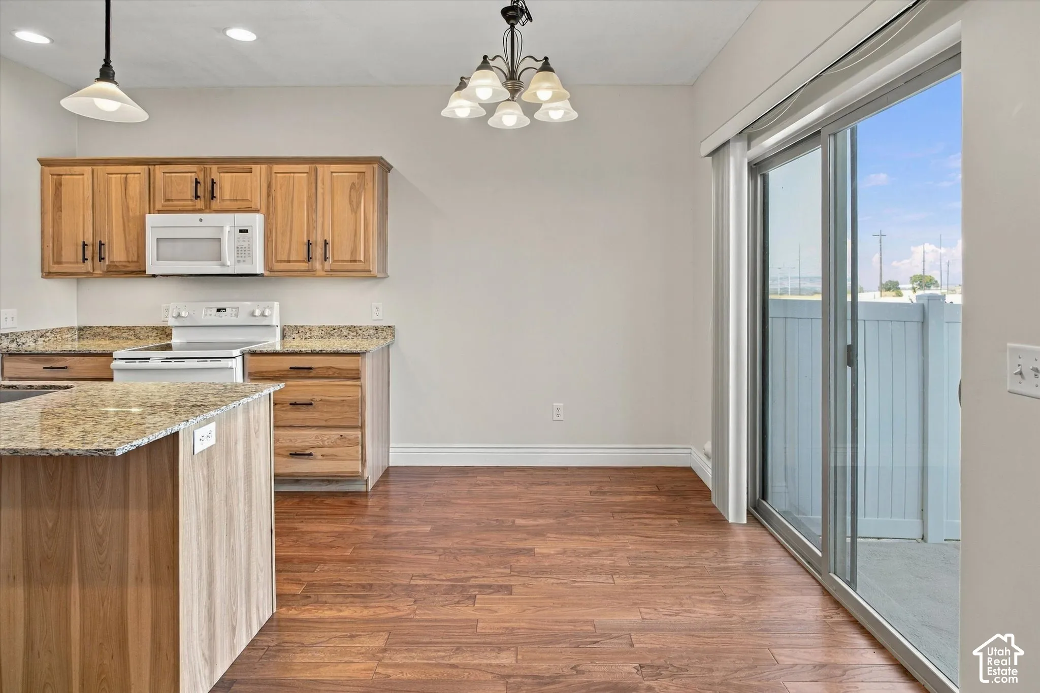 Wood-finish flooring throughout, kitchen featuring wood cabinetry, granite-style countertops, and white appliances
