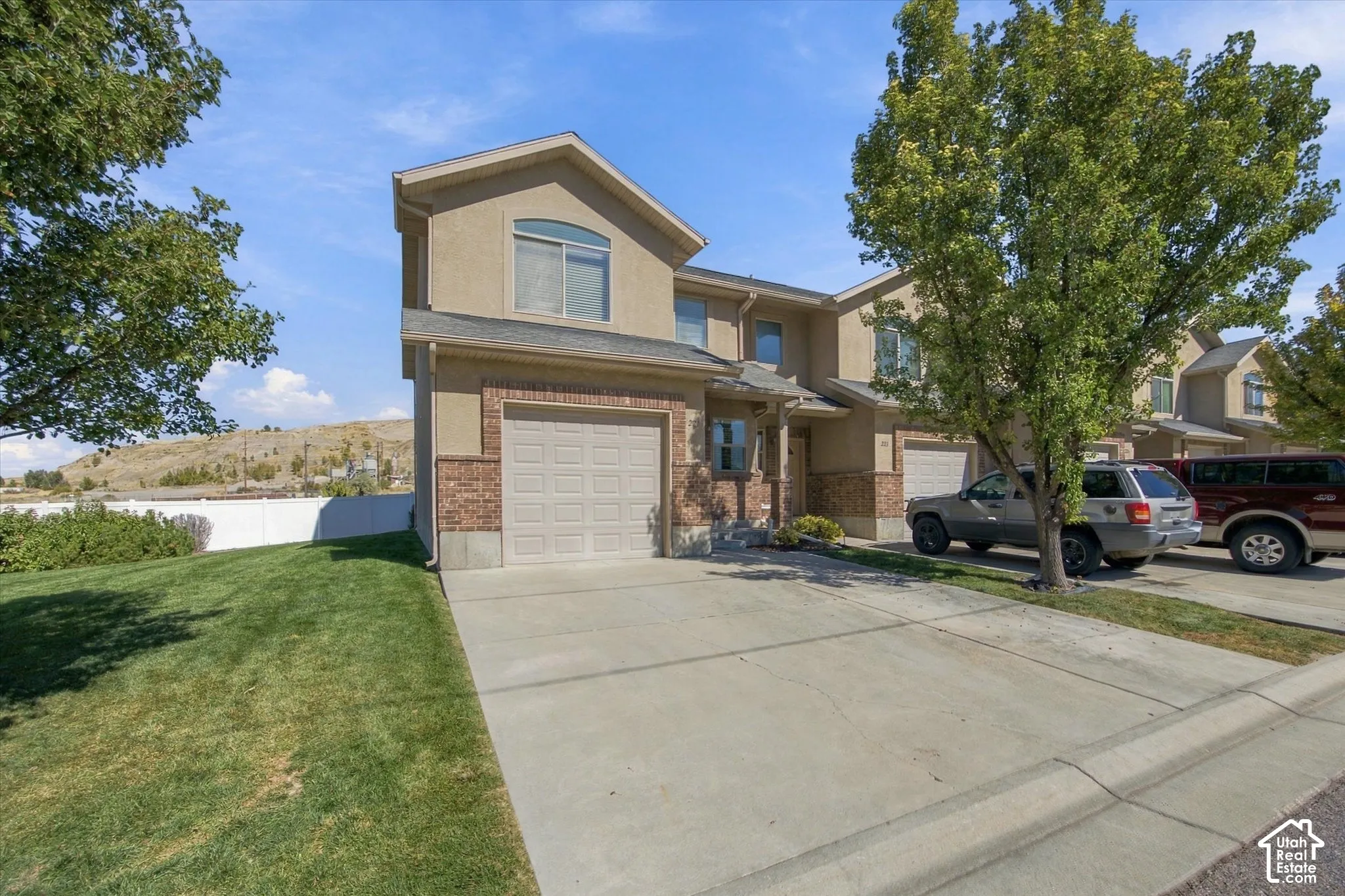 Stucco exterior with brick detailing, attached garage, concrete driveway, and front lawn