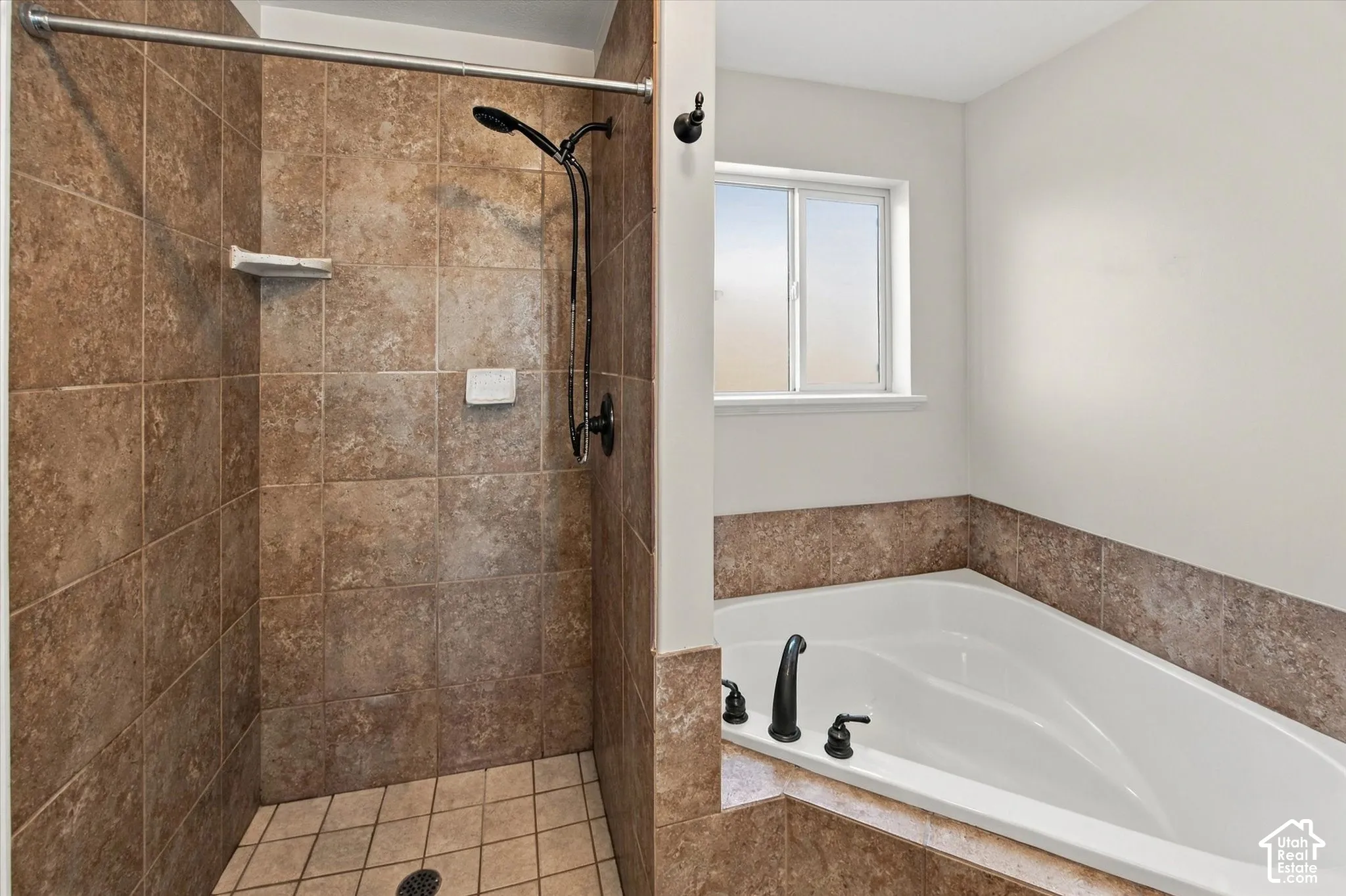 Tiled shower stall with a matte black shower head, accompanied by a built-in soaking tub featuring matte black fixtures and a privacy window