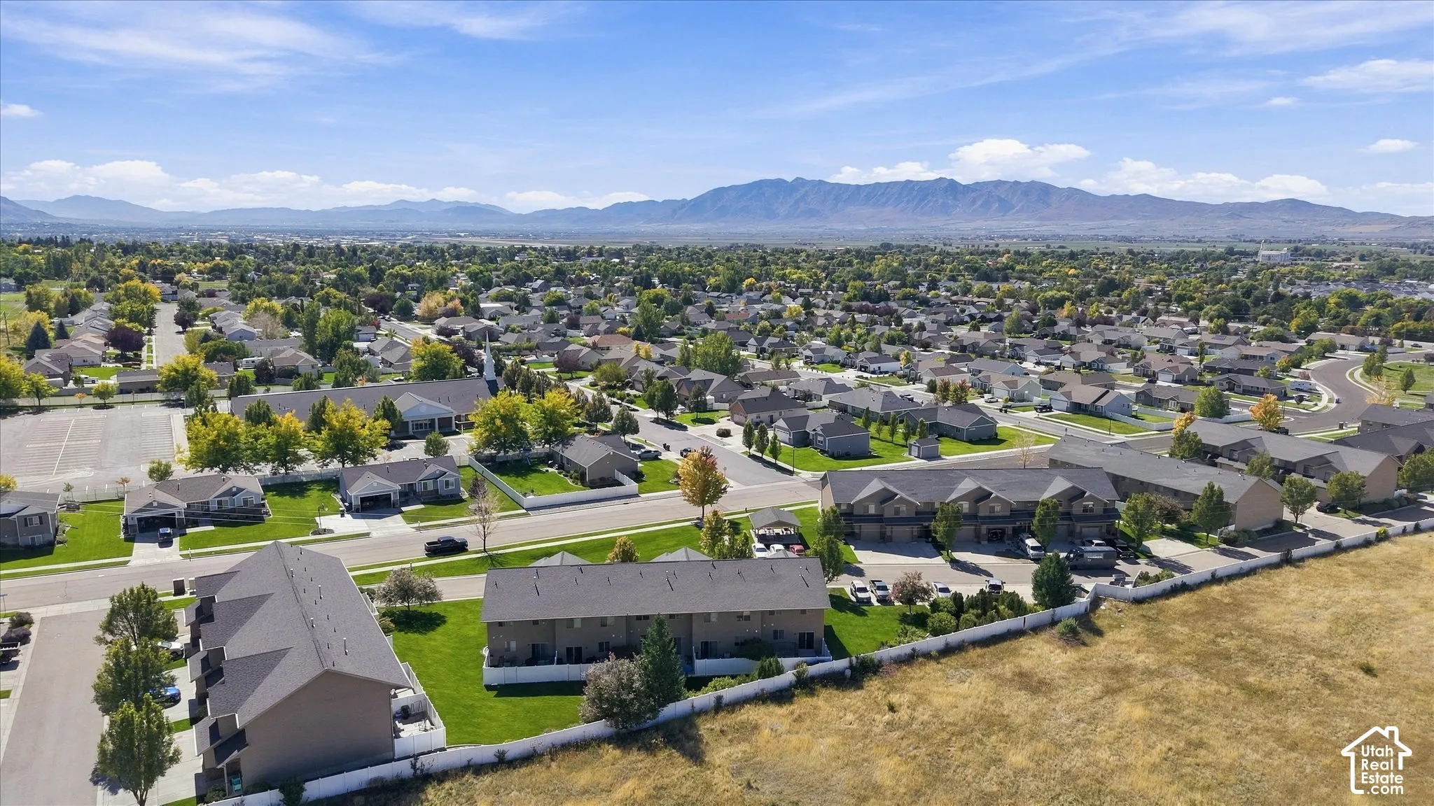 Expansive residential area featuring numerous single-family homes and multi-unit buildings, mature trees, and mountain scenery in the background