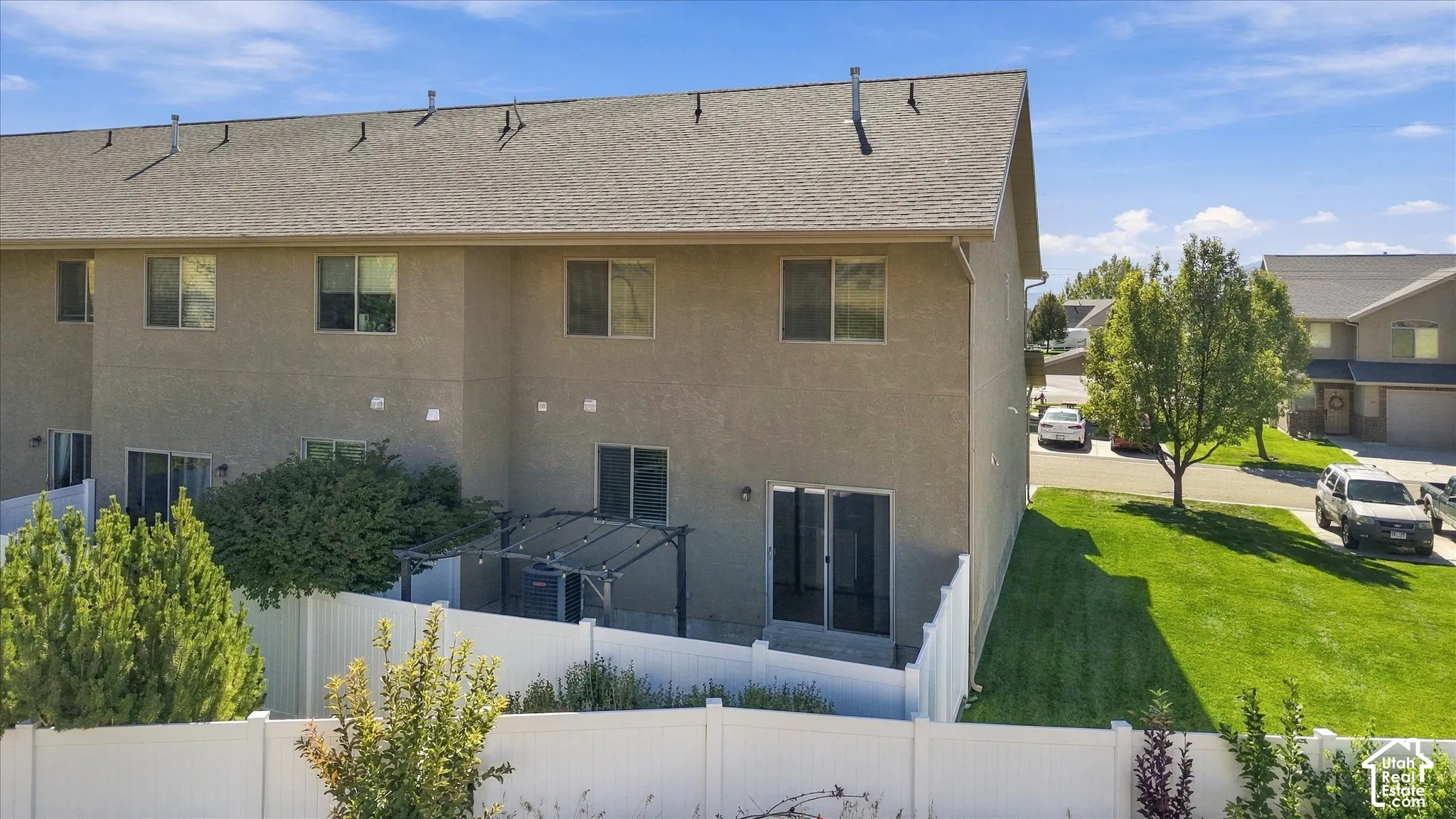 Rear exterior featuring stucco siding, multiple windows, a white privacy fence, and a patio with a pergola