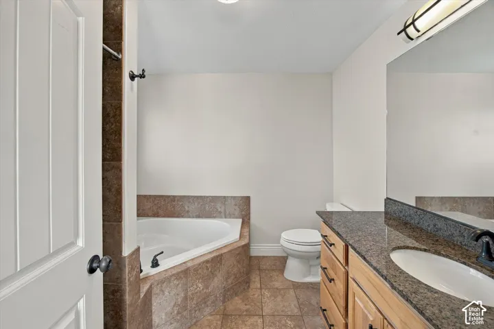 Corner soaking tub with tiled surround, wood vanity with integrated sink, granite-style countertop, and wall-mounted mirror