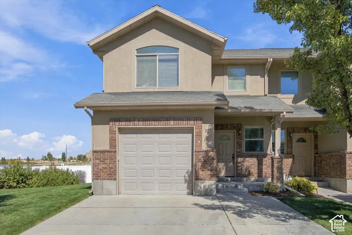 Stucco and brick exterior with an attached garage, paved driveway, and mature landscaping