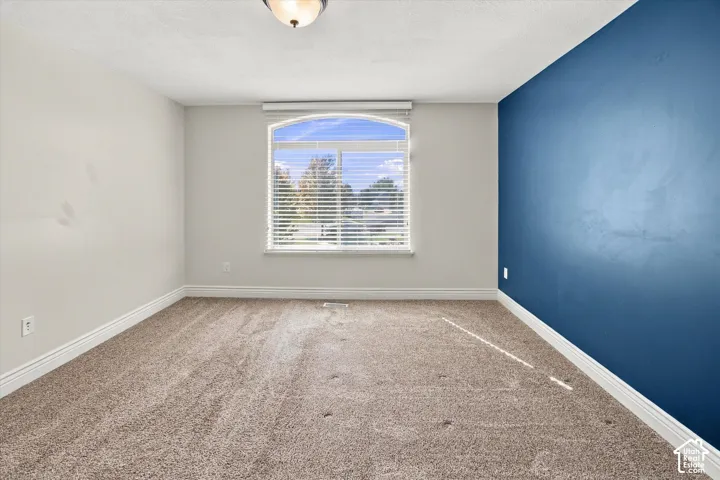 Arched window with blinds, recessed ceiling light, wall-to-wall carpeting, and a contrasting accent wall