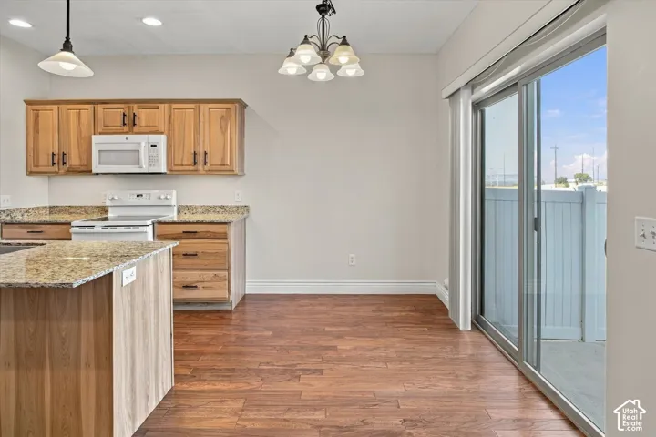 Wood-finish flooring throughout, kitchen featuring wood cabinetry, granite-style countertops, and white appliances