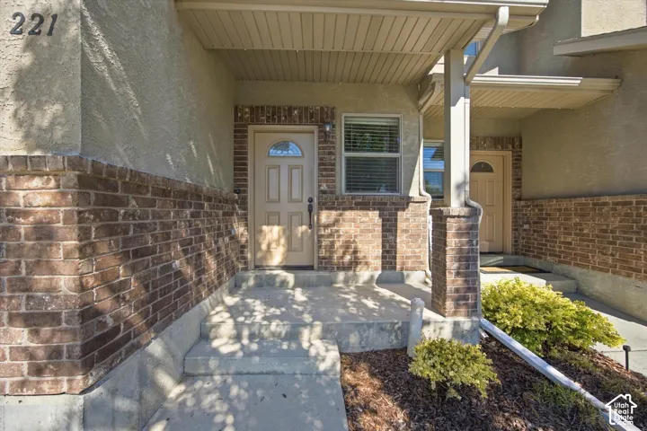 Stucco and brick exterior with a covered entry, concrete steps, and a window with blinds