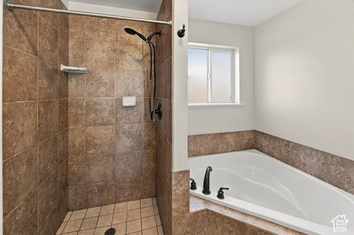 Tiled shower stall with a matte black shower head, accompanied by a built-in soaking tub featuring matte black fixtures and a privacy window