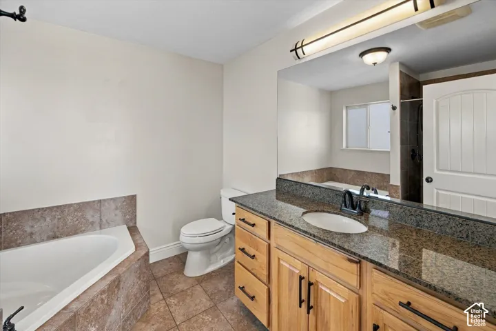 Bathroom featuring a corner soaking tub with tile surround, a wood-finish vanity with a dark stone countertop, and a recessed single-basin sink
