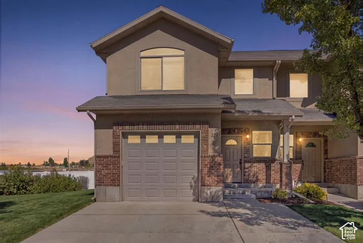 Stucco and brick exterior with a front entry garage, mature landscaping, and concrete driveway