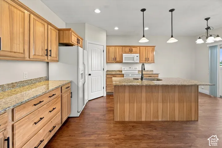 Kitchen featuring wood-finish cabinetry, stone countertops, stainless steel appliances, and a central island with a sink
