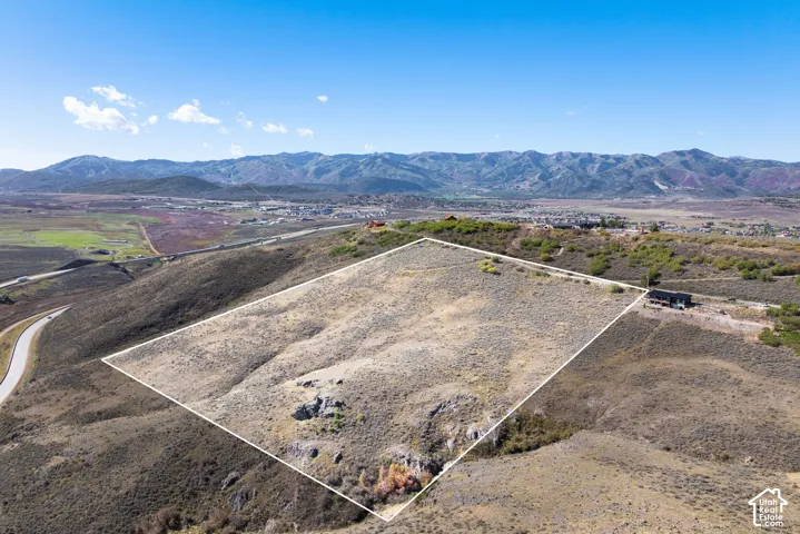 Expansive undeveloped lot with natural ground cover, visible mountain range backdrop, and distant highway access