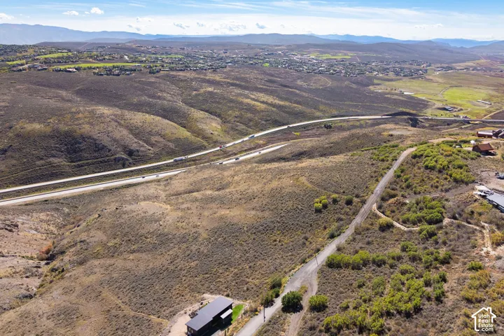 Expansive arid landscape with a distant residential development, a multi-lane highway, and a winding unpaved road