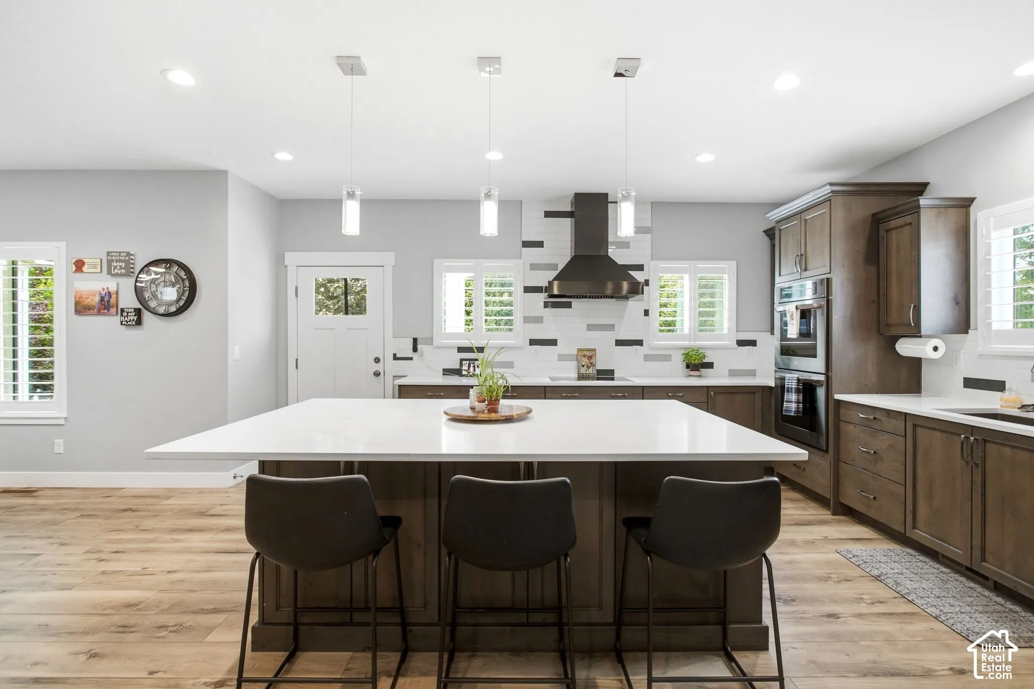 Spacious kitchen featuring a large central island with seating, pendant lighting, stainless steel double ovens, and wood-finish cabinetry