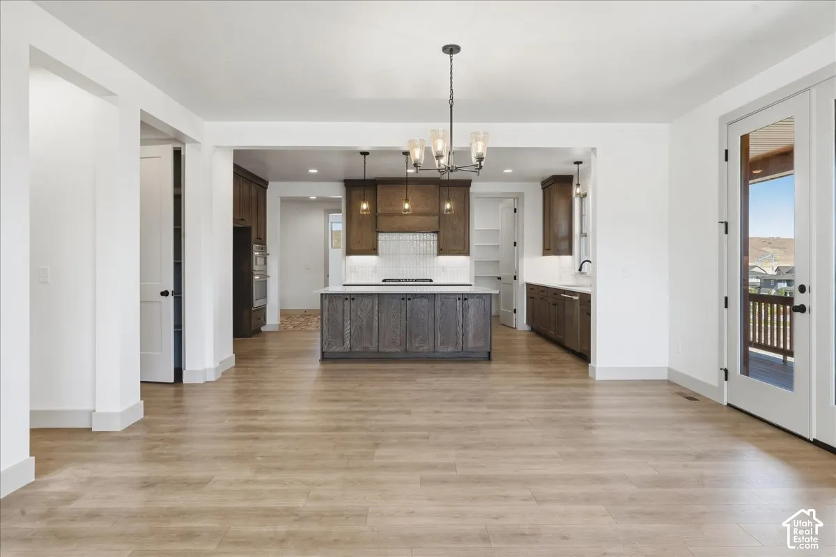 Open-concept living space with wood-finish flooring, a kitchen island, pendant lighting, and double-paned glass doors