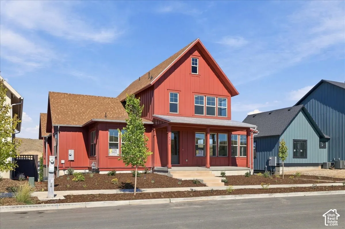 Red board and batten exterior with a covered front porch, multi-pane windows, and a shingled roof