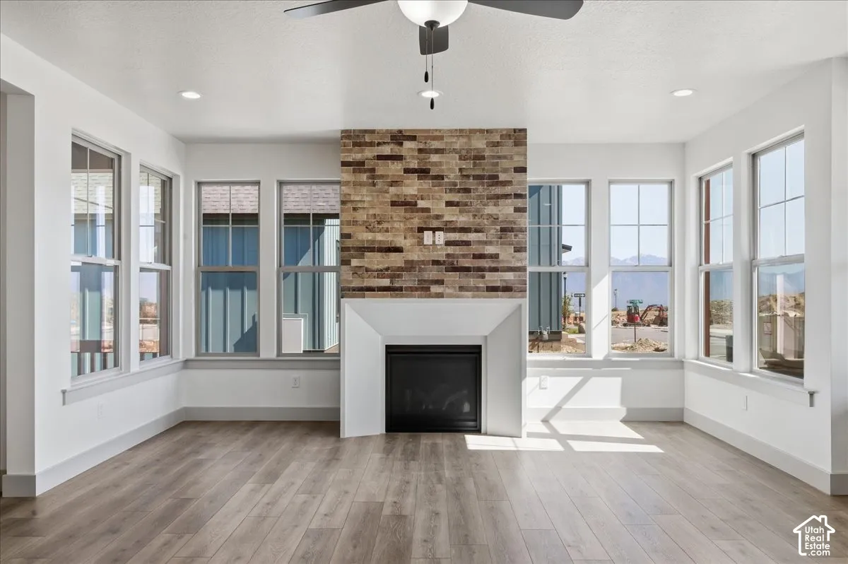 Spacious room featuring wood-finish flooring, a contemporary fireplace with a stacked stone facade and white mantel, recessed lighting, and multiple large windows