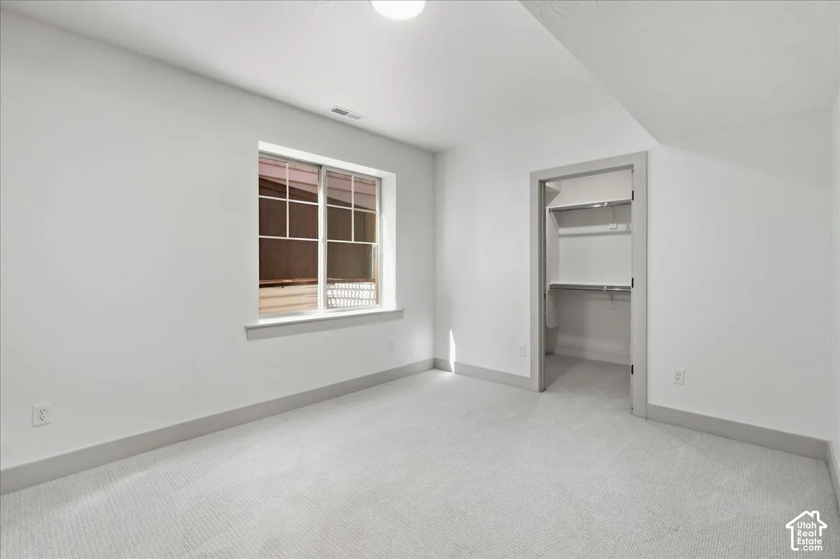 White wall paint, light-colored carpet flooring, recessed ceiling light, built-in closet shelving, and a window with white trim