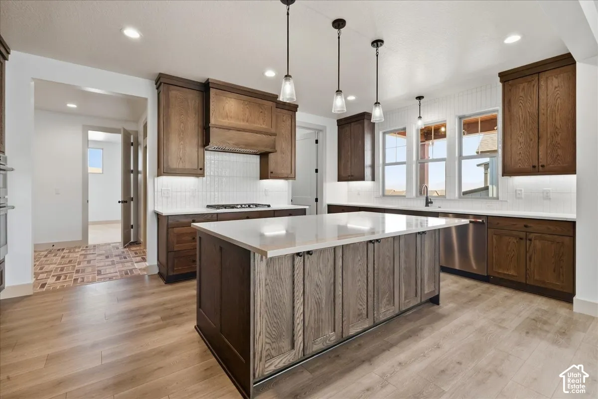 Gourmet kitchen with a large island, wood-finish cabinetry, stainless steel appliances, pendant lighting, and light wood-finish flooring