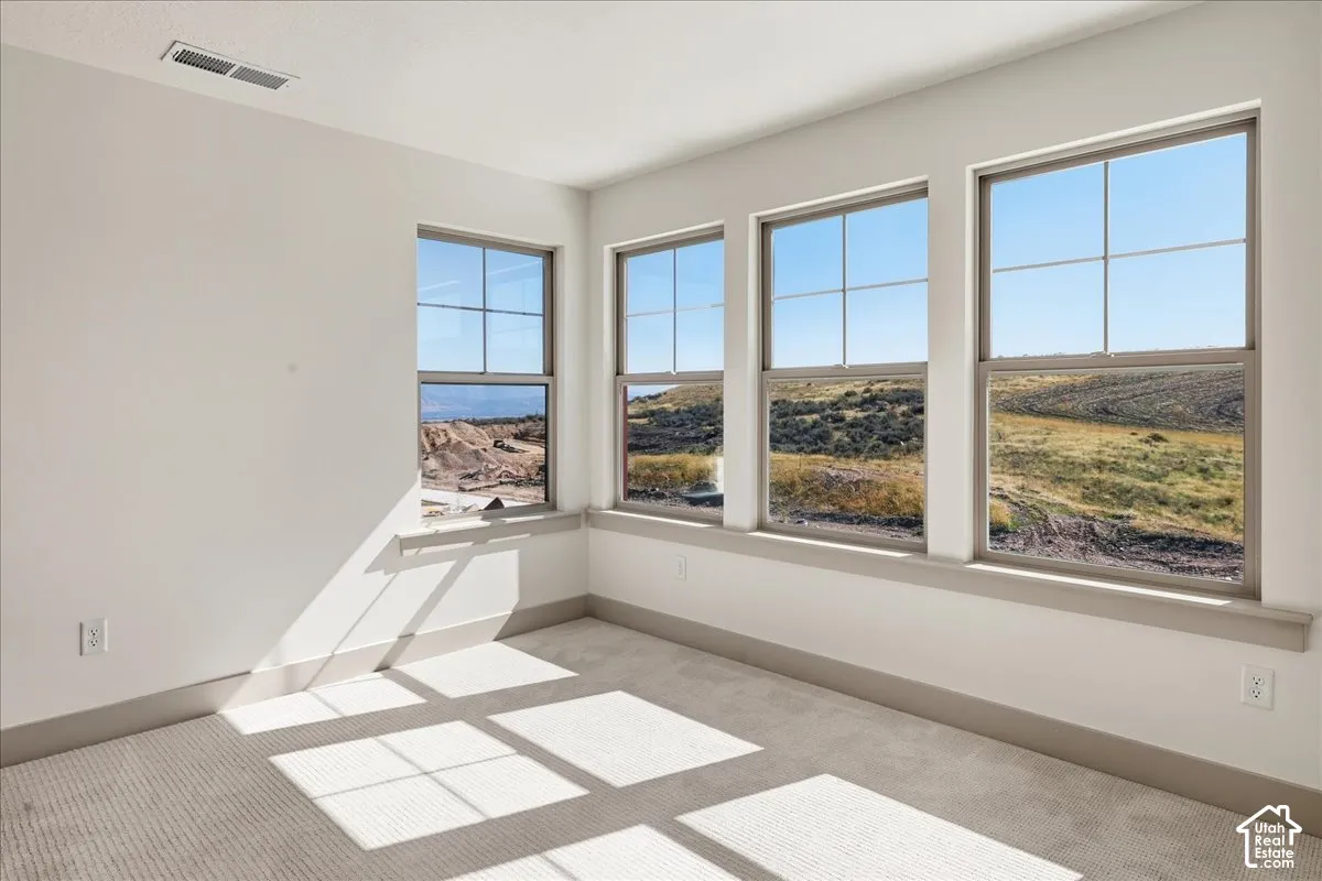 Upstairs guest bedroom 1. Multiple grid-pane windows with trim, light wall color, and carpeted flooring