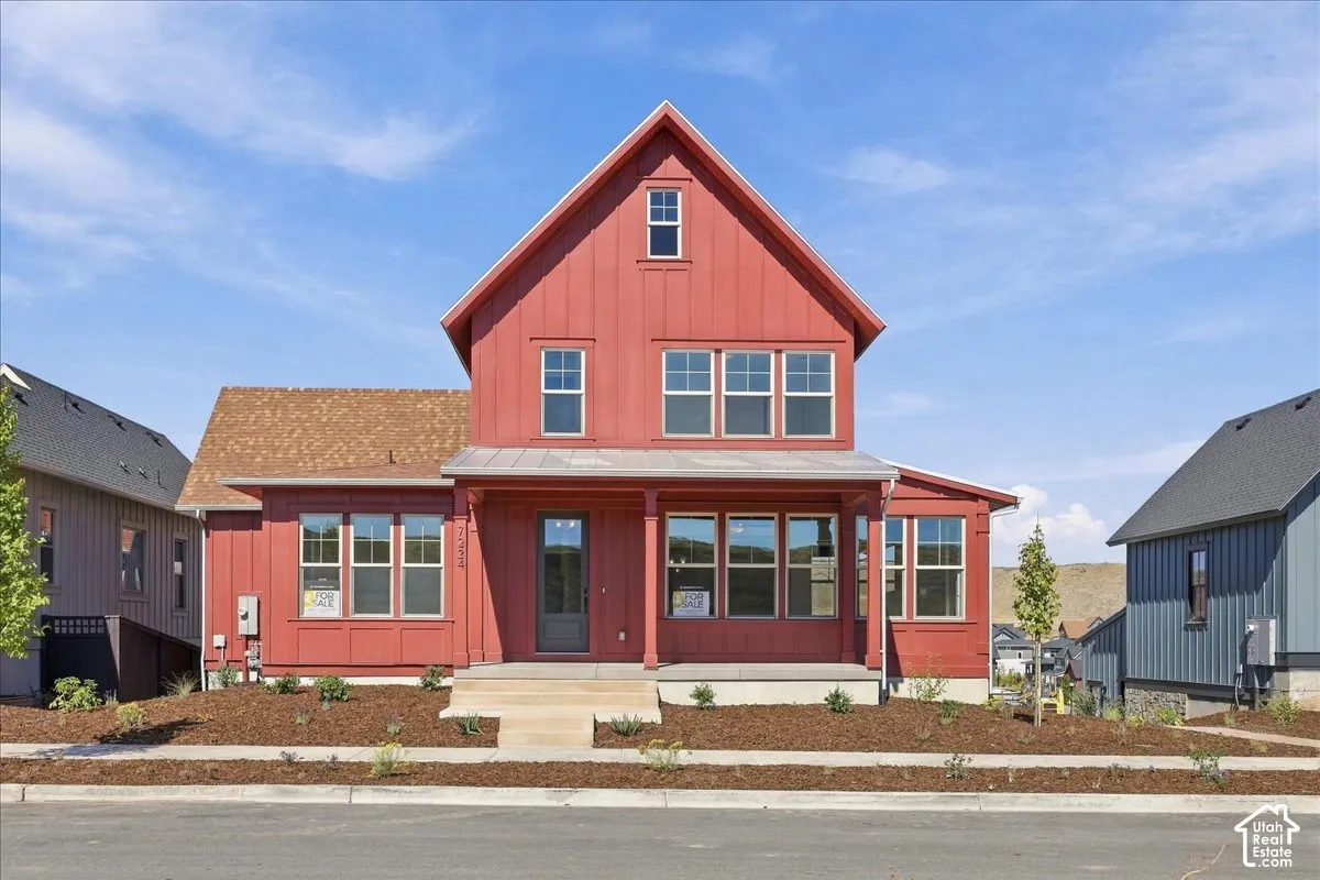 Two-story farmhouse style exterior featuring red vertical siding, a covered front porch, and multiple windows
