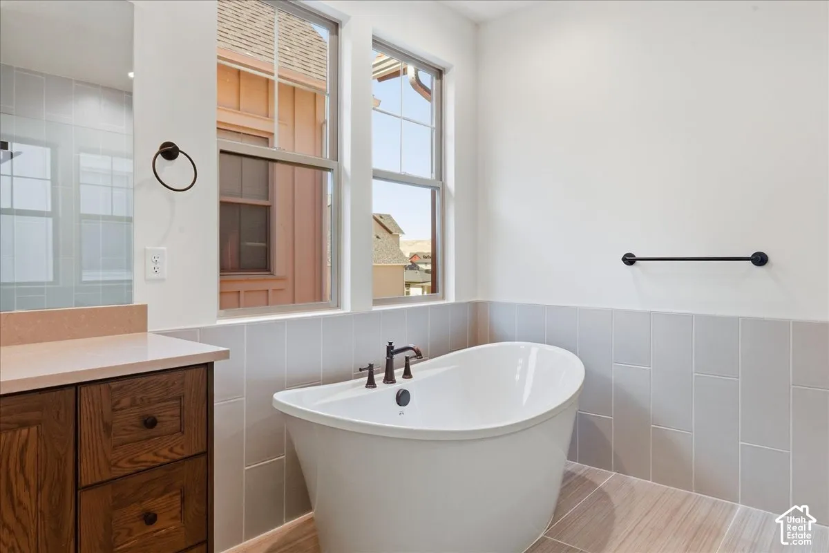Freestanding soaking tub with dark bronze fixtures, wood-finish flooring, and light gray wall tile