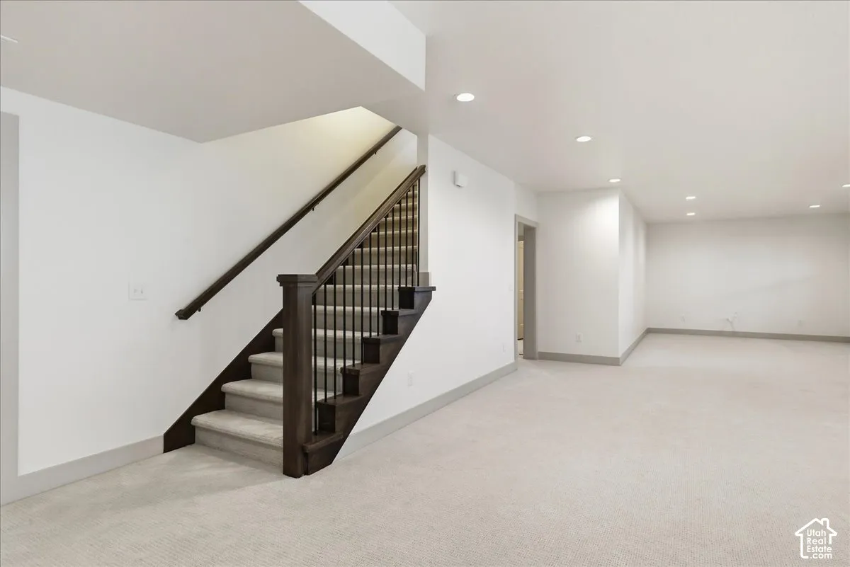 Spacious room with recessed lighting, light-toned carpeting, and a dark wood staircase with black balusters