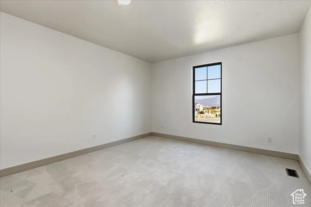 Main Floor rec room above garage. White walls with a single window and light-colored carpet