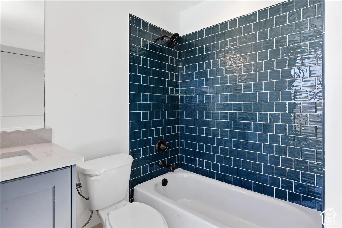 Ensuite barhroom White bathtub with a deep blue subway tile surround, matte black shower fixtures, a white toilet, and a vanity featuring a light-colored countertop and dark blue cabinetry