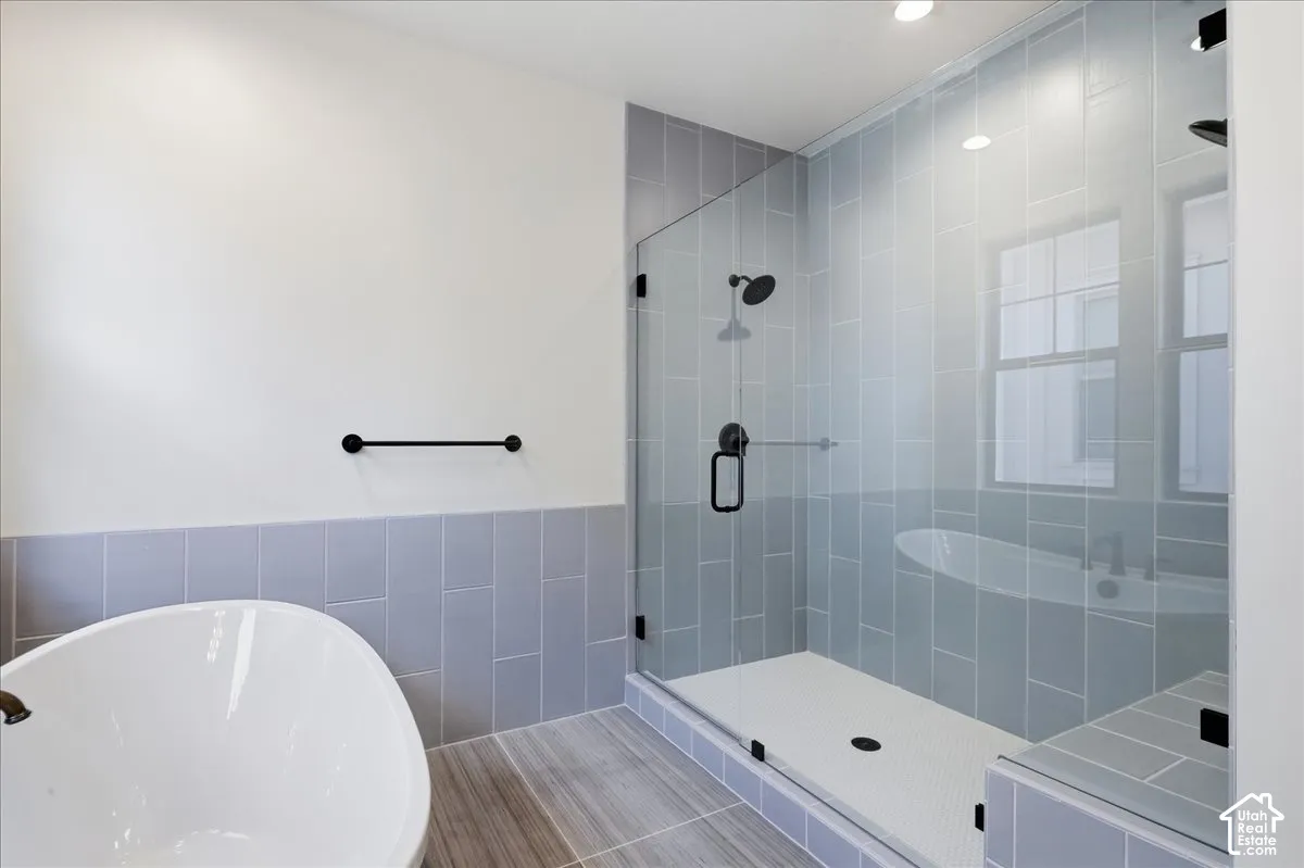 Freestanding soaking tub, glass-enclosed shower, tiled shower walls, shower bench, and wood-finish flooring