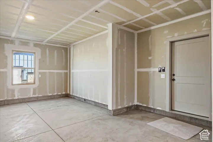 Interior space with concrete flooring, unfinished drywall, a single window, and a door