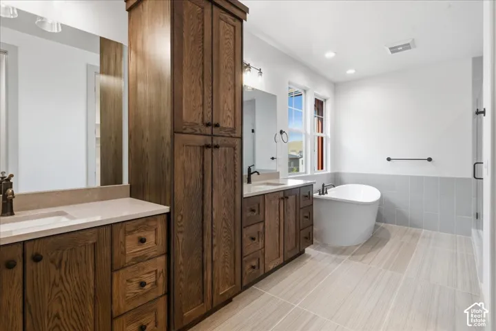 Primary Bathroom Wood-finish cabinetry with multiple storage options, dual vanity sinks, light-toned stone countertops, a freestanding soaking tub, and a glass-enclosed shower