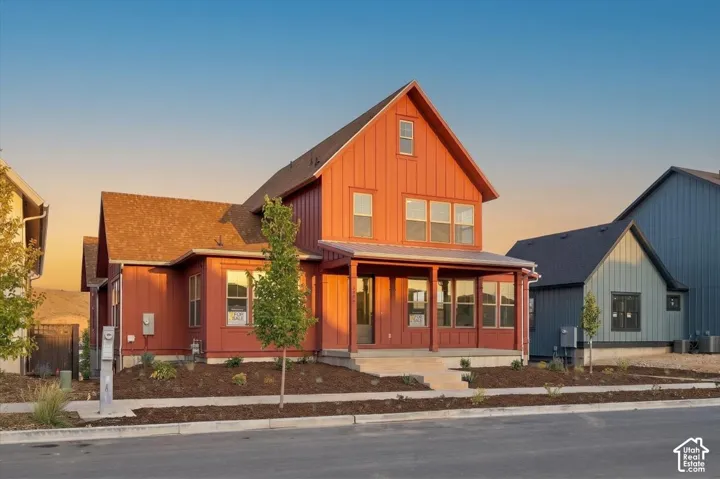 Red board and batten exterior with a covered front porch, asphalt shingle roof, and multiple windows