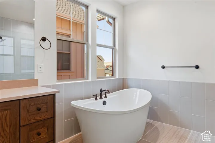 Freestanding soaking tub with dark bronze fixtures, wood-finish flooring, and light gray wall tile