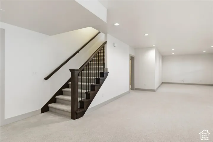 Spacious room with recessed lighting, light-toned carpeting, and a dark wood staircase with black balusters