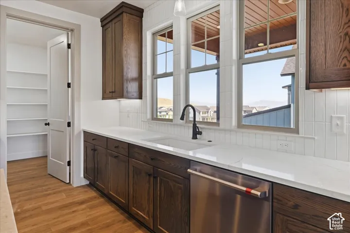 Dark wood-finish cabinetry, light countertops, wood-finish flooring, white tile backsplash, and a built-in pantry with shelving