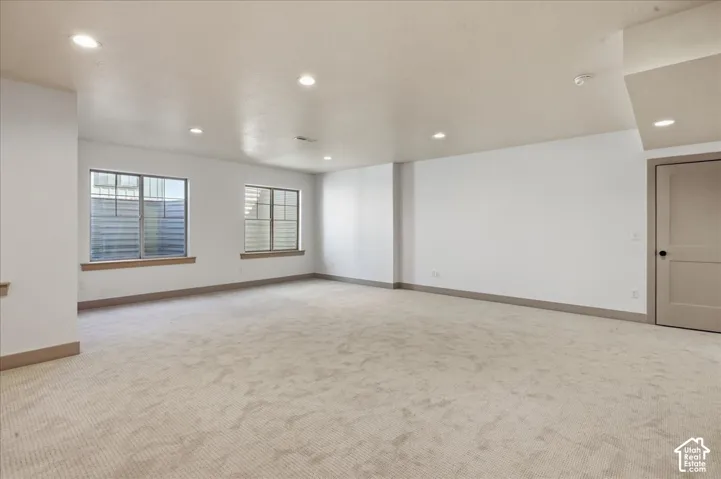 Spacious room featuring neutral carpeting, recessed lighting, and two windows with wood-finish sills