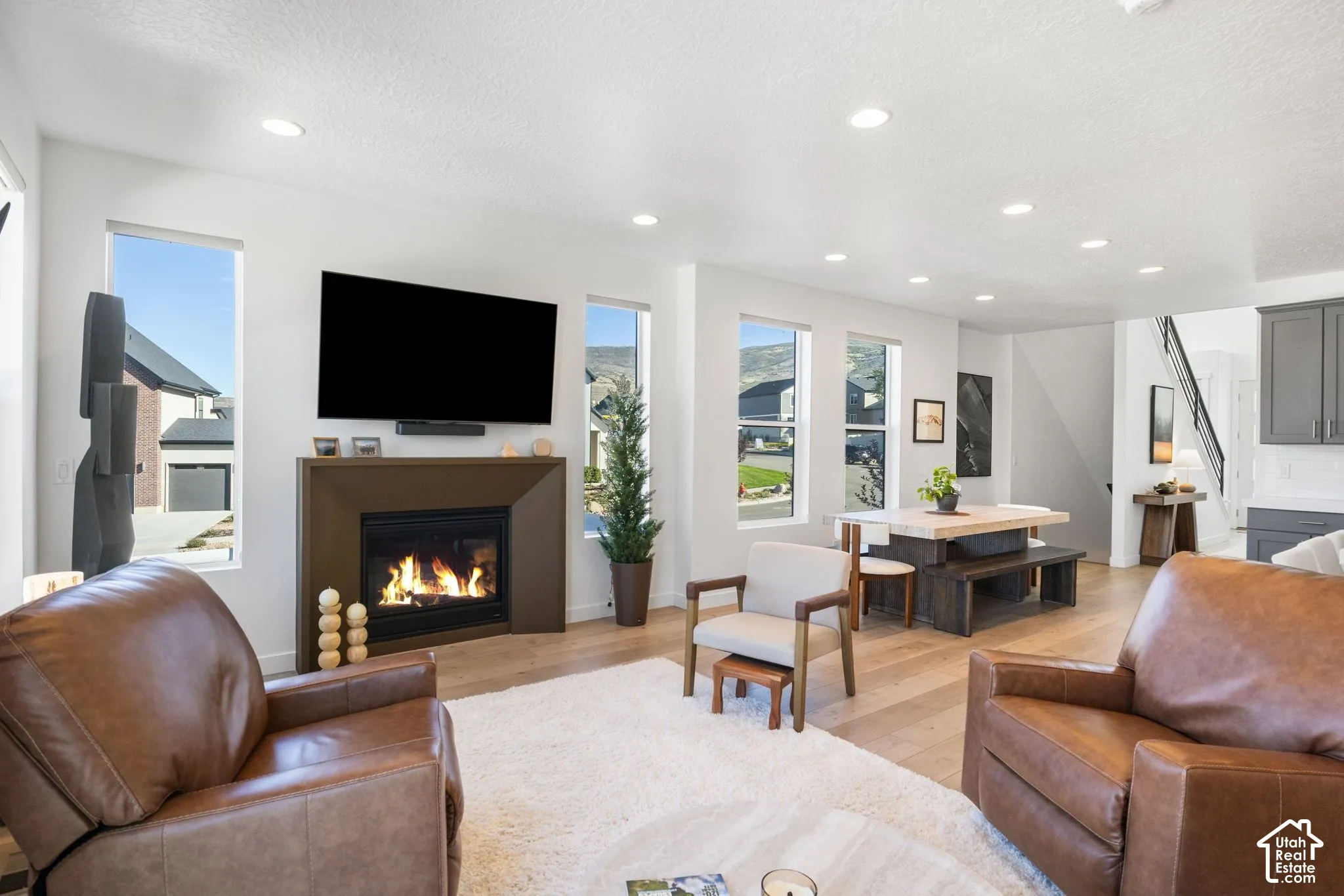 Fireplace with a brown surround, recessed lighting, wood-finish flooring, multiple windows, and a staircase with a black handrail