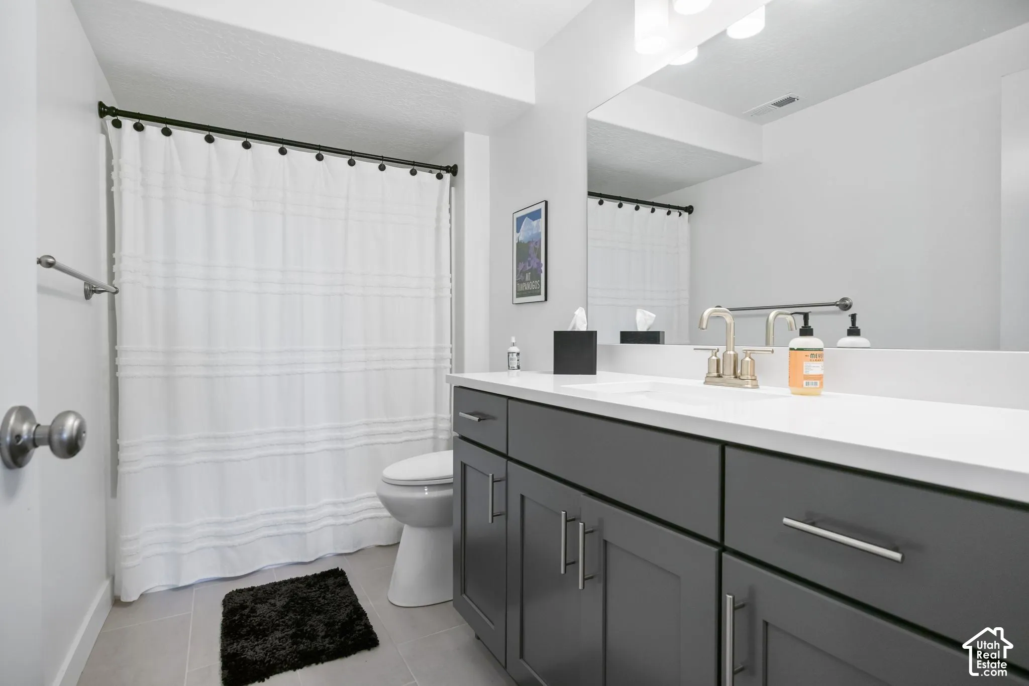 Vanity with a white countertop and dark gray cabinetry, brushed nickel faucet, large wall-mounted mirror, and overhead vanity lighting